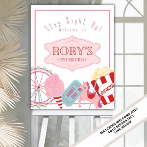 May include: A pink and white welcome sign for a carnival themed first birthday party. The sign says "Step Right Up! Welcome to Rory's First Birthday". The sign features a Ferris wheel, cotton candy, popcorn, a ticket, and a carousel horse.