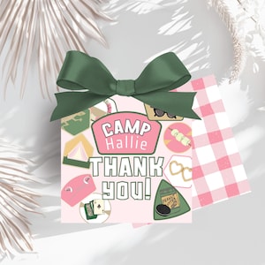 May include: A pink gift box with a green bow, featuring the text "CAMP Hallie THANK YOU!". The box is decorated with camping-themed illustrations, including a tent, sunglasses, and a peanut butter sandwich.