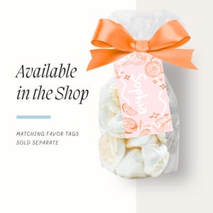 Peut inclure: Un sac transparent rempli de meringues blanches, nou&eacute; avec un ruban orange. Une &eacute;tiquette rose avec le nom "Sophia" et des illustrations d'agrumes est attach&eacute;e. Le texte de l'image indique "Disponible dans la boutique" et "&Eacute;tiquettes de faveur assorties vendues s&eacute;par&eacute;ment."