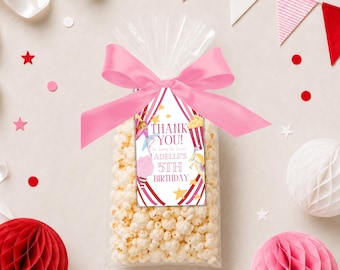 May include: A clear cellophane bag filled with popcorn, tied with a pink ribbon and a tag that reads "THANK YOU!" and "Adelle's 5th Birthday". The tag has a circus theme with red and white stripes and star accents.