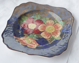 May include: A blue and white ceramic plate with a floral design. The plate features three pink and red flowers with yellow centers. The plate has a scalloped edge.