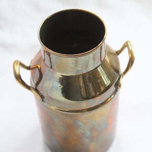 May include: A small, antique-looking brass milk can with two handles. The can has a worn, aged finish with a golden hue.