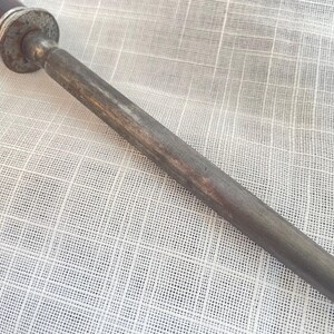 May include: Close-up of a steel knife sharpening tool with a dark brown handle and a textured, cylindrical metal rod. The tool has a worn, vintage appearance.
