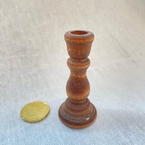 May include: A small wooden candle holder with a brown finish. The holder has a round base and a tall, slender stem.