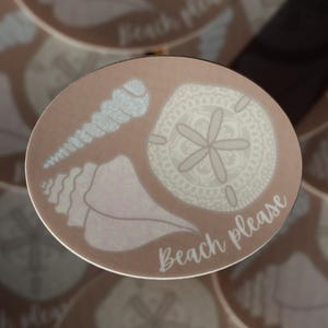 May include: A set of four brown coasters with a white seashell design and the text "Beach Please".