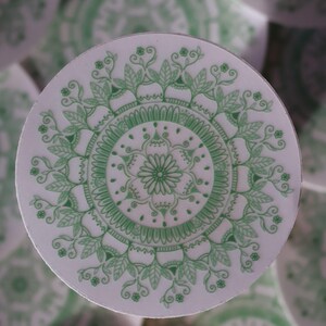 May include: A white round sticker with a green mandala design. The mandala features intricate floral patterns and a central flower.