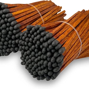 May include: Two bundles of wooden matches. Each match has a dark gray head and a brown wooden stick. The matches are bound together with a thin, clear elastic band. The background is white.