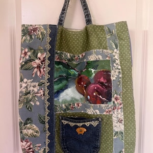 Op de afbeelding: Een patchwork tote bag met een denim zak en een schilderij van kersen. De tas heeft bloemen- en stippenstof in tinten blauw, groen en wit. De handvatten zijn gemaakt van denim.