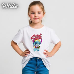 May include: A white t-shirt featuring a cartoon character with the word "Stitch" in red and pink. The character is blue and wearing headphones. The word "White" is in the upper left corner.