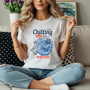Peut inclure: T-shirt blanc avec le texte "Keep Chilling and Let Your Problems Go". Le graphisme représente un squelette se relaxant dans un bain de glace bleu. Le t-shirt est de style décontracté et confortable.
