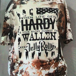 May include: A white tie-dye t-shirt with a black graphic print that reads "When life gets HARDY & your backs against the WALLEN keep JELLY ROLLIN".