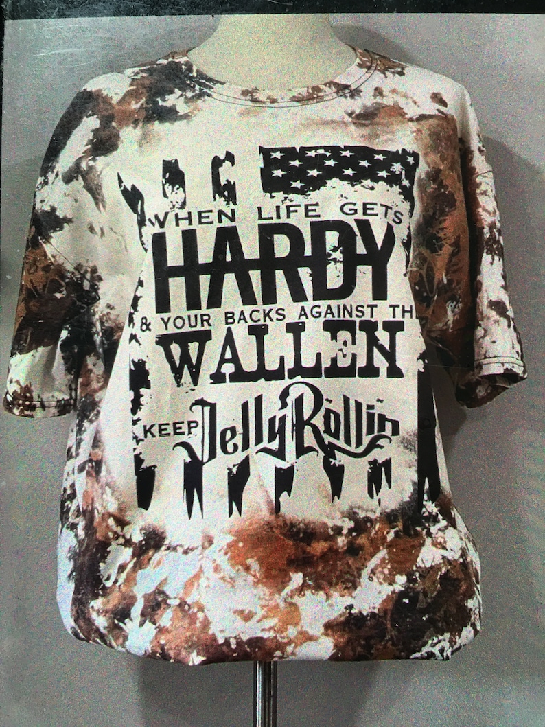 May include: A white tie-dye t-shirt with a black graphic print that reads "When life gets HARDY & your backs against the WALLEN keep JELLY ROLLIN".