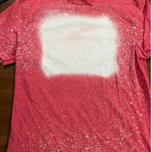 May include: Red t-shirt with a white bleach design. The design is a rectangle with a faded, speckled look.