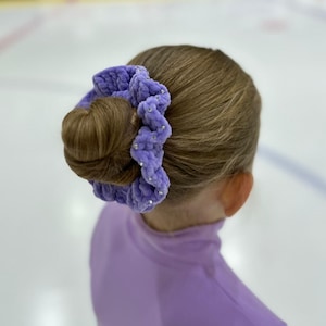 May include: A purple fuzzy hair scrunchie with small rhinestones. The scrunchie is holding a bun of brown hair.