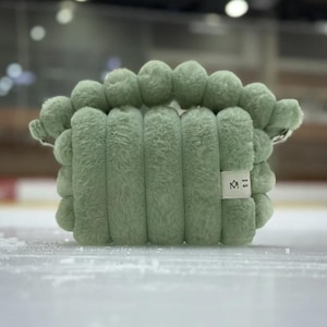 May include: A sage green plush pillow with a rounded shape and a small white label with the text "some spirit" and a logo.