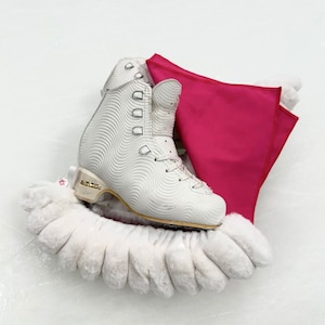 Op de afbeelding: Witte kunstschaats met een witte bonten laarshoes en een roze stoffen hoes. De laars heeft een wit golvend patroon en een gouden rand.