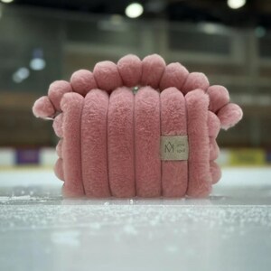 May include: A pink plush pillow with a rounded top and a textured, ribbed design. The pillow has a small brown label with the text "arme spot" and a stylized "M" logo.