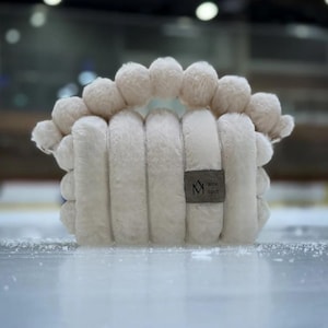 May include: White fluffy pillow with a pom-pom trim and a small logo that says "amie spot" in a brown font.