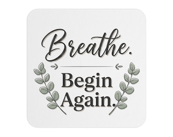 Könnte beinhalten: Ein quadratischer weißer Untersetzer mit dem schwarzen Text "Breathe. Begin Again." in der Mitte. Das Design zeigt zwei symmetrische grüne Eukalyptuszweige, die den Text flankieren, sowie eine dünne horizontale Linie zwischen den beiden Phrasen.