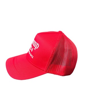 May include: Red and white trucker hat with the text "Trump 2024" and "America Back" on the front.