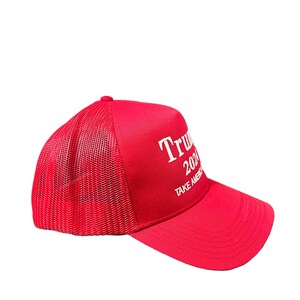 May include: Red mesh trucker hat with white embroidered text that reads "Trump 2024 Take America Back".
