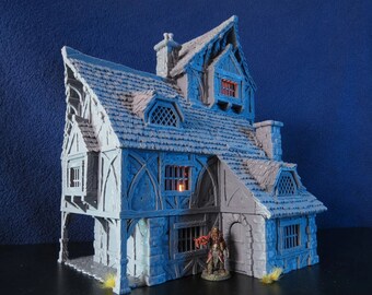 May include: A miniature fantasy house in grey and blue. The house has a detailed roof, windows, and a small figure in front. The house has a medieval architectural style, with a chimney and decorative trim. The house is lit from within.