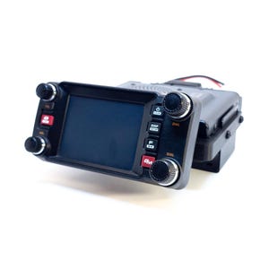 May include: A black handheld radio transceiver with a screen, multiple buttons, and a dial. The radio has a black and gray mounting bracket.