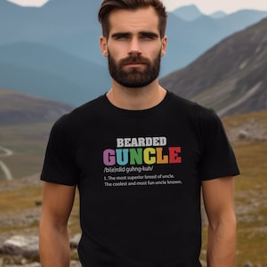 May include: A black t-shirt with a colorful graphic that reads "BEARDED GUNCLE /bi(e)rdid guhng-kuh/ 1. The most superior breed of uncle. The coolest and most fun uncle known."