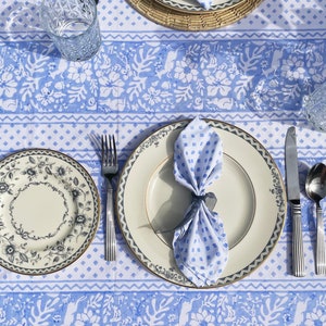 May include: A blue and white patterned tablecloth with a white plate, a blue and white napkin, a fork, a knife, and a spoon. The plate has a black and white floral design.