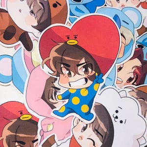 May include: A collection of colorful cartoon character stickers. The stickers feature various characters in different outfits and poses. The central sticker shows a character in a blue onesie with yellow polka dots, a red heart-shaped hat, and a cheerful expression.