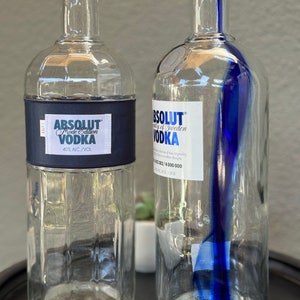 Puede incluir: Dos botellas de vidrio transparente de Absolut Vodka. La botella de la izquierda tiene una etiqueta negra con texto blanco que dice "Absolut Vodka Mode Edition 40% Alc./Vol.". La botella de la derecha tiene una franja azul alrededor de la botella y una etiqueta blanca con texto negro que dice "Absolut Vodka of Sweden".