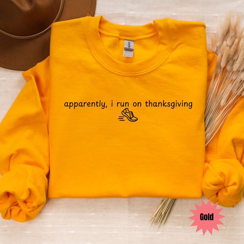 May include: Mustard yellow sweatshirt with the text "apparently, i run on thanksgiving" and a running shoe graphic in black. The long-sleeved crewneck shirt is a casual style.