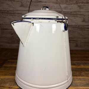 May include: White enamelware coffee pot with a blue trim and a metal handle. The vintage pot has a spout and a lid with a small knob. The pot shows signs of wear, adding to its antique charm. The pot is approximately 25 cm tall.