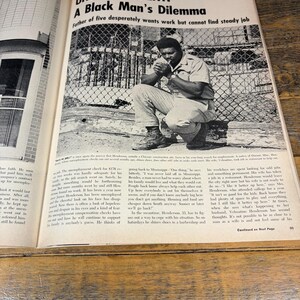 K&ouml;nnte beinhalten: Ein schwarz-wei&szlig; Magazin-Doppelseite mit dem Titel "UNEMPLOYMENT: A Black Man's Dilemma". Das Bild zeigt einen Mann, der drau&szlig;en sitzt und raucht, mit Text, der seinen Kampf um Arbeit und die Versorgung seiner Familie beschreibt.