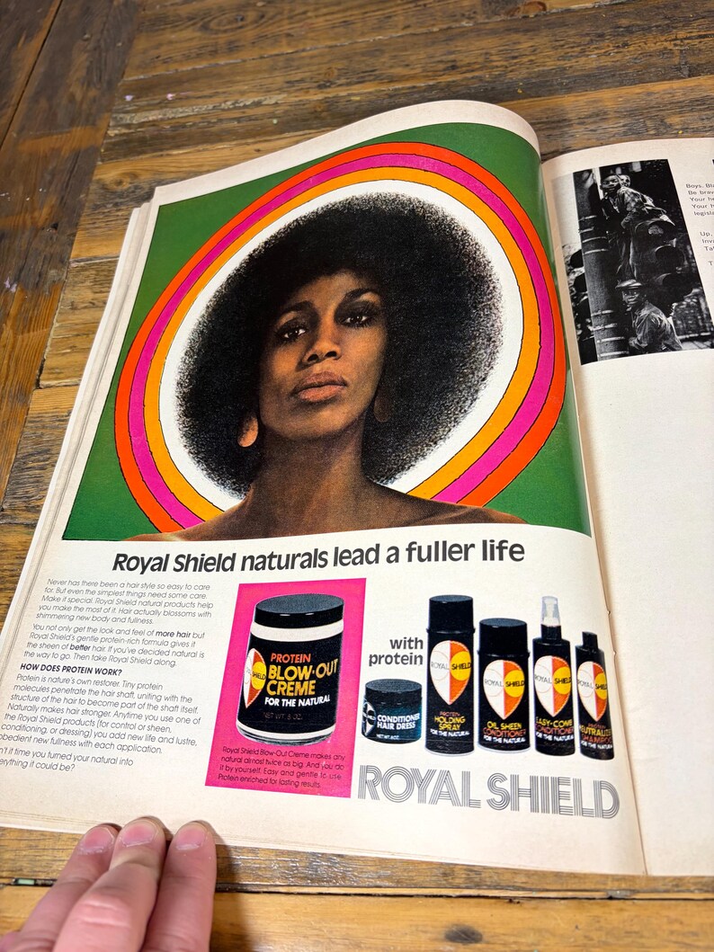 K&ouml;nnte beinhalten: Vintage-Werbung f&uuml;r Royal Shield Haarprodukte. Die Anzeige zeigt eine Frau mit einer gro&szlig;en Afro-Frisur, umrahmt von einem farbenfrohen kreisf&ouml;rmigen Design. Verschiedene Haarpflegeprodukte werden gezeigt, darunter Protein Blow-Out Creme und Holding Spray.