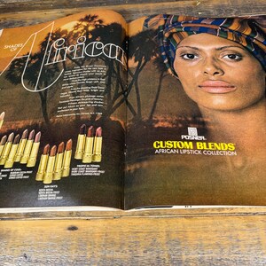 K&ouml;nnte beinhalten: Eine Doppelseite einer Zeitschrift mit einer Frau mit Kopftuch und einer Lippenstiftkollektion. Der Text lautet "Shades of Africa" und "Custom Blends African Lipstick Collection". Die Lippenstifte sind in goldenen Tuben mit verschiedenen Farbt&ouml;nen.