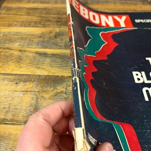 K&ouml;nnte beinhalten: Eine Vintage-Augustausgabe des Ebony-Magazins. Das Cover hat einen dunkelblauen Hintergrund mit roten, gr&uuml;nen und wei&szlig;en Akzenten. Der Titel des Magazins, "EBONY", ist in Rot und Wei&szlig; dargestellt.