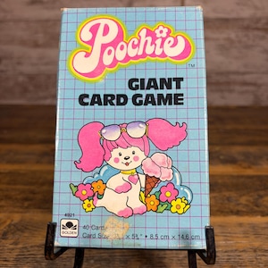 May include: A vintage "Poochie" Giant Card Game box. The box features a cartoon dog character with pink hair and sunglasses, holding an ice cream cone. The box is light blue with a grid pattern and the text "Poochie" and "Giant Card Game". The card size is 3 x 5 ½ inches.
