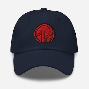 Könnte beinhalten: Eine marineblaue Baseballkappe mit einem roten gestickten Logo eines stilisierten Buchstabens "R" in einem Kreis.