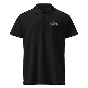 May include: Black polo shirt with a collared neckline and short sleeves. The shirt features a three-button placket and a white Cessna logo on the left chest. A classic and versatile garment.