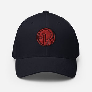 Könnte beinhalten: Marineblaue Baseballkappe mit einem roten, gestickten, kreisförmigen Logo. Das Logo zeigt einen stilisierten Buchstaben "B" und die Zahl "13". Die Kappe hat einen gebogenen Schirm und eine strukturierte Passform.