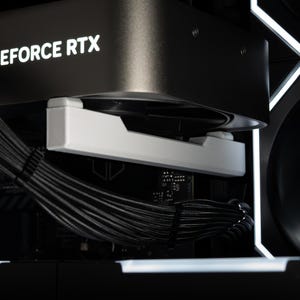 Puede incluir: Primer plano de una tarjeta gráfica de ordenador negra con el texto blanco "GEFORCE RTX". Se ve un soporte blanco. Los cables negros están agrupados. El fondo es oscuro con iluminación LED blanca.