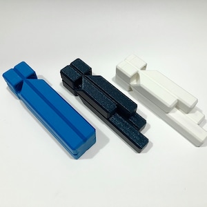 Puede incluir: Tres silbatos de plástico en azul, negro y blanco. Los silbatos están apilados uno encima del otro.