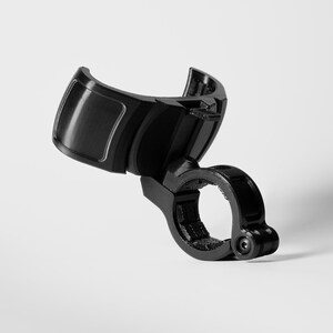 A professionally shot GO Plus + compatible handlebar mount, rugged edition, in gloss black. This angled product shot on a white background highlights the curved snap-fit cradle and the secure circular clamp at the base. The durable mounting accessory is designed to hold a circular mobile gaming auto-catcher on handlebars for bikes, scooters, and strollers, providing a stable, hands-free solution for active players.