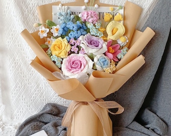 Puede incluir: Un ramo de flores de ganchillo en varios colores, incluyendo rosa, amarillo, azul y blanco, envuelto en papel marrón y atado con una cinta de arpillera.