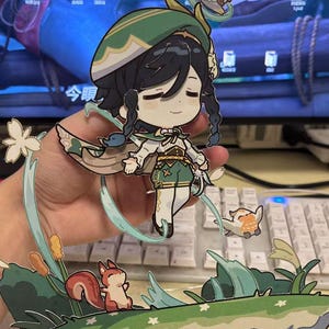 May include: A papercraft figurine of a girl with long dark hair wearing a green hat and a white dress. She is holding a small white bird in her hand. The figurine is surrounded by green leaves and flowers.