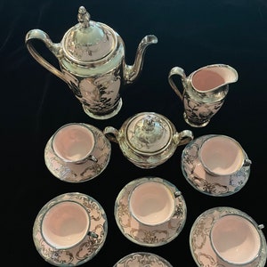 May include: A vintage tea set with a pink and silver design. The set includes a teapot, creamer, sugar bowl, and six teacups and saucers.