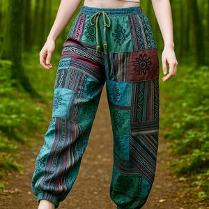 May include: Patchwork harem pants in teal, burgundy, and green with floral and geometric patterns. The pants have a drawstring waist and elastic ankles. The image shows the pants on a person walking on a path in a forest.