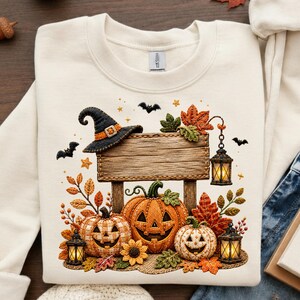 Könnte beinhalten: Cremefarbenes Sweatshirt mit Halloween-Design. Das Design zeigt einen Hexenhut, geschnitzte Kürbisse, Laternen und Herbstblätter. Ein Holzschild ist ebenfalls enthalten, mit Fledermäusen und Sternen, die das Design umgeben.