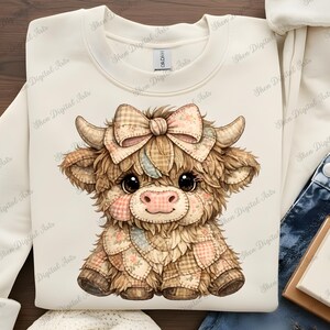 Könnte beinhalten: Cremefarbenes Sweatshirt mit einer Illustration einer Highland-Kuh. Die Kuh hat ein Patchwork-Design und eine große Schleife. Das Design beinhaltet sanfte Farben und eine niedliche Ästhetik. Der Text "Shen Digital Arts" ist sichtbar.